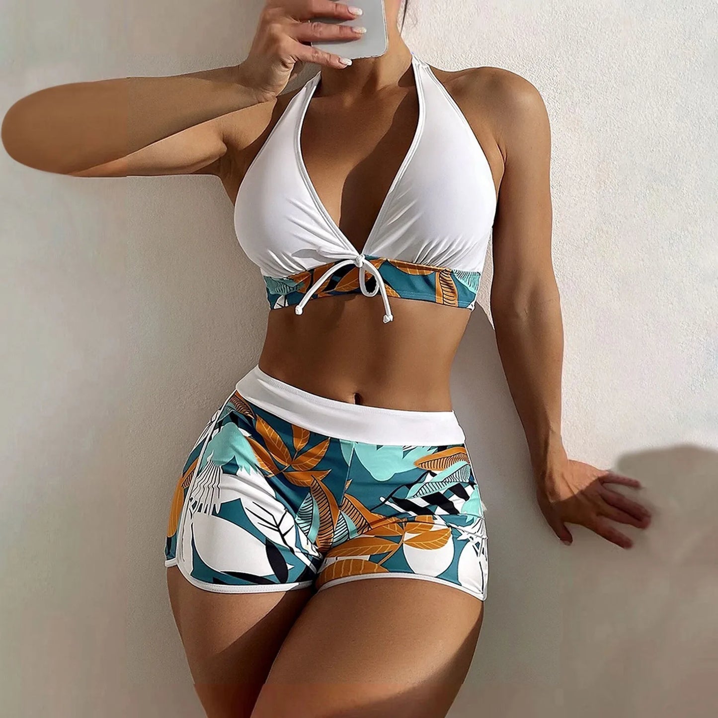 Woman wearing a white High Waist Plant Print Bikini Set top and colorful floral shorts against a plain background