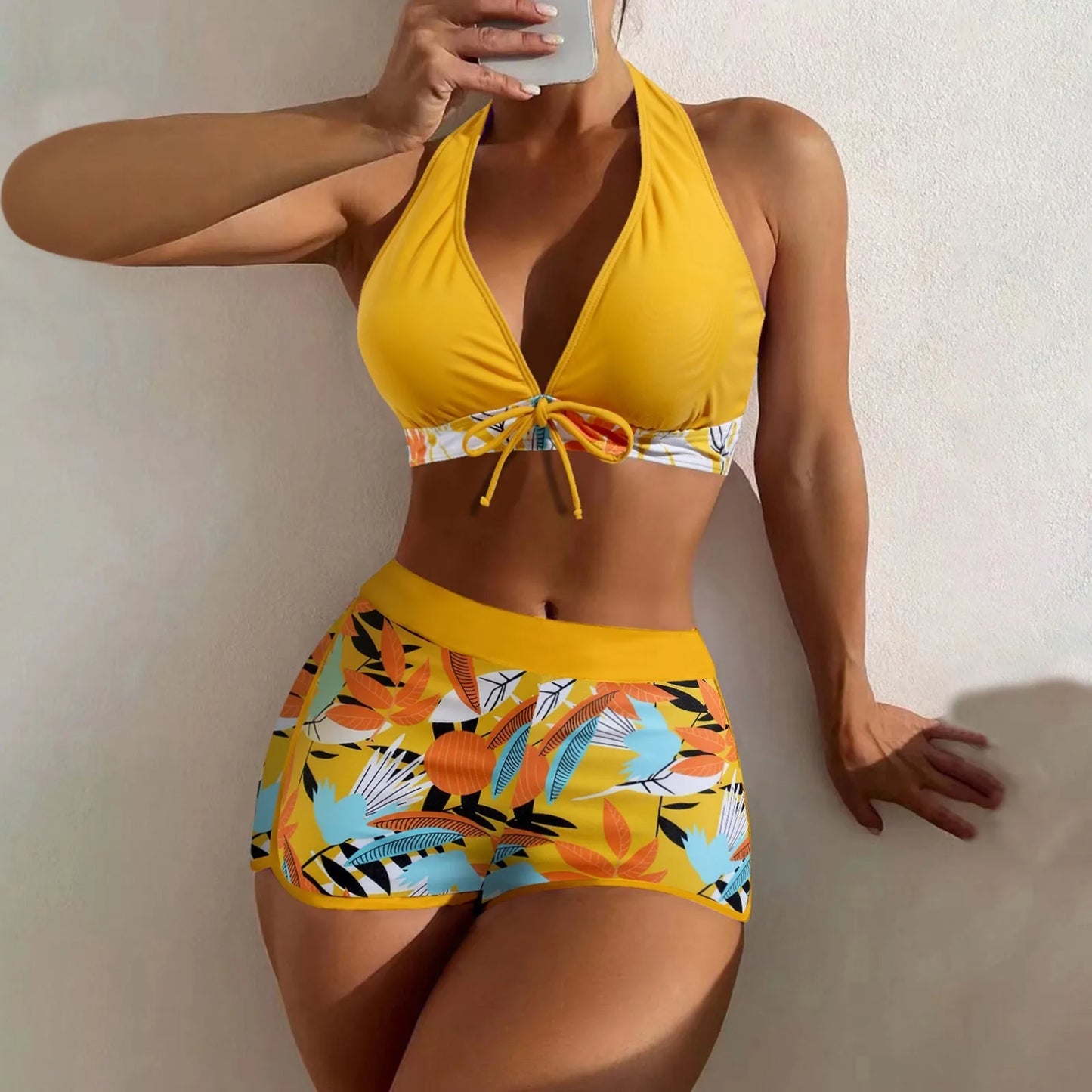 Woman wearing a yellow bikini with floral patterned bottom against a plain background