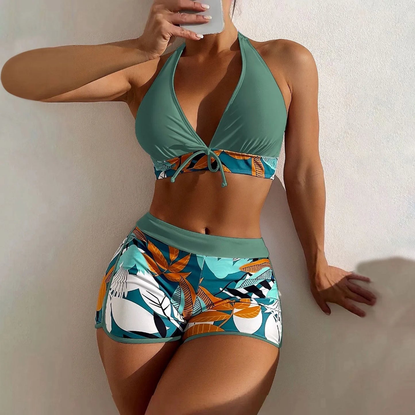 Woman wearing a green and patterned two-piece swimsuit against a plain background