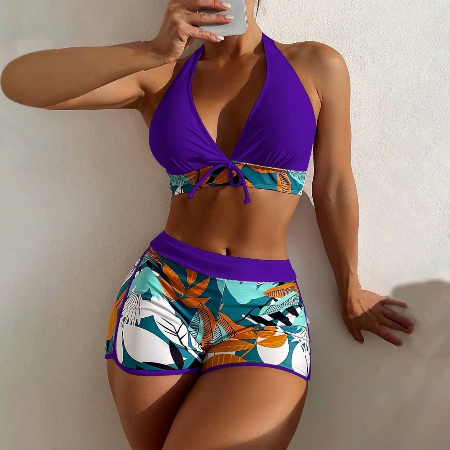 Person wearing a colorful bikini with a purple top and tropical leaf patterned bottom against a plain background.