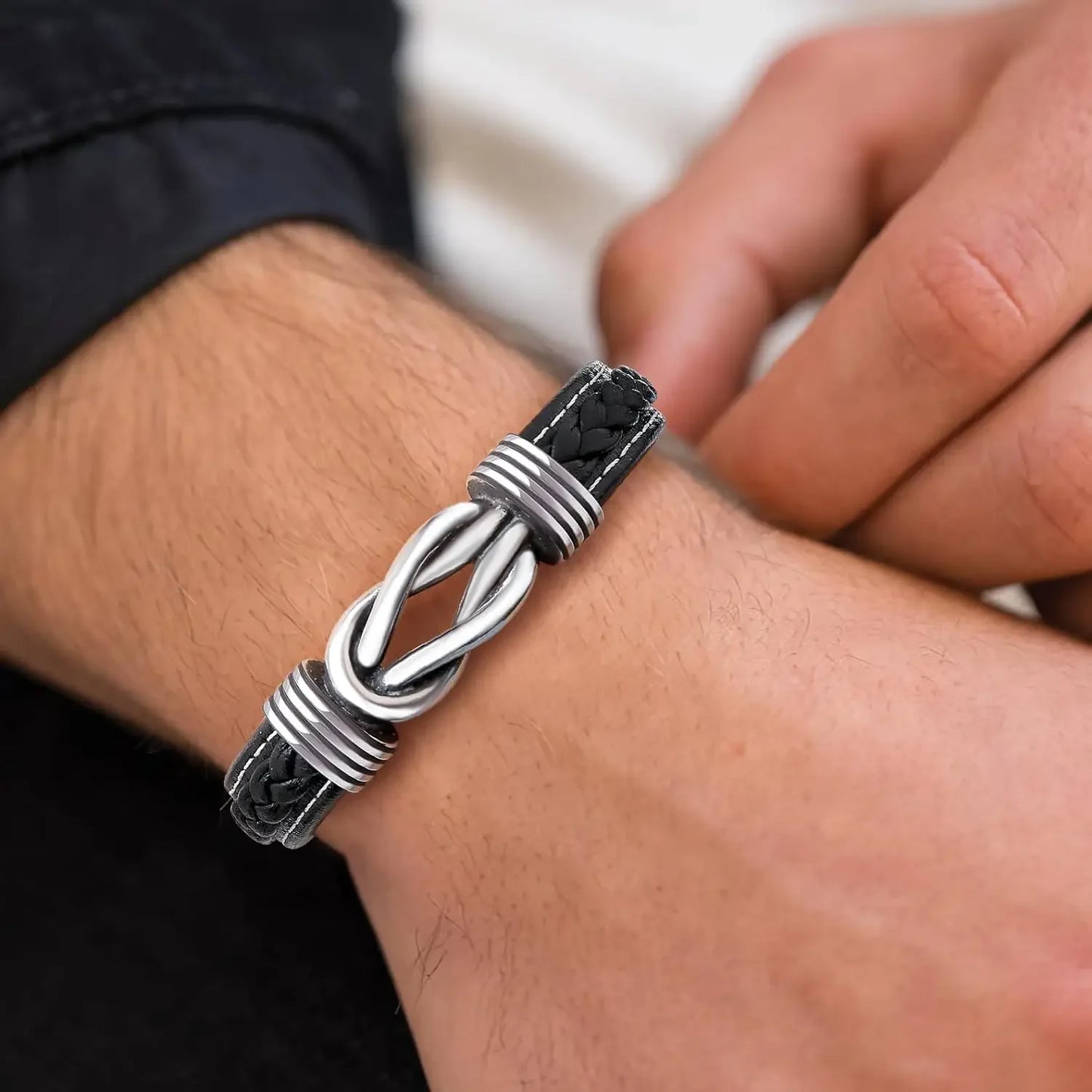 A man showcases a silver bracelet paired with a stylish black leather band on his wrist.