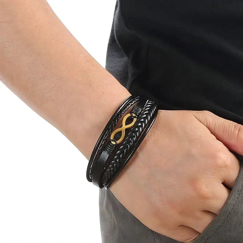 A man showcases a black leather bracelet adorned with a gold clasp on his wrist, highlighting a stylish accessory.