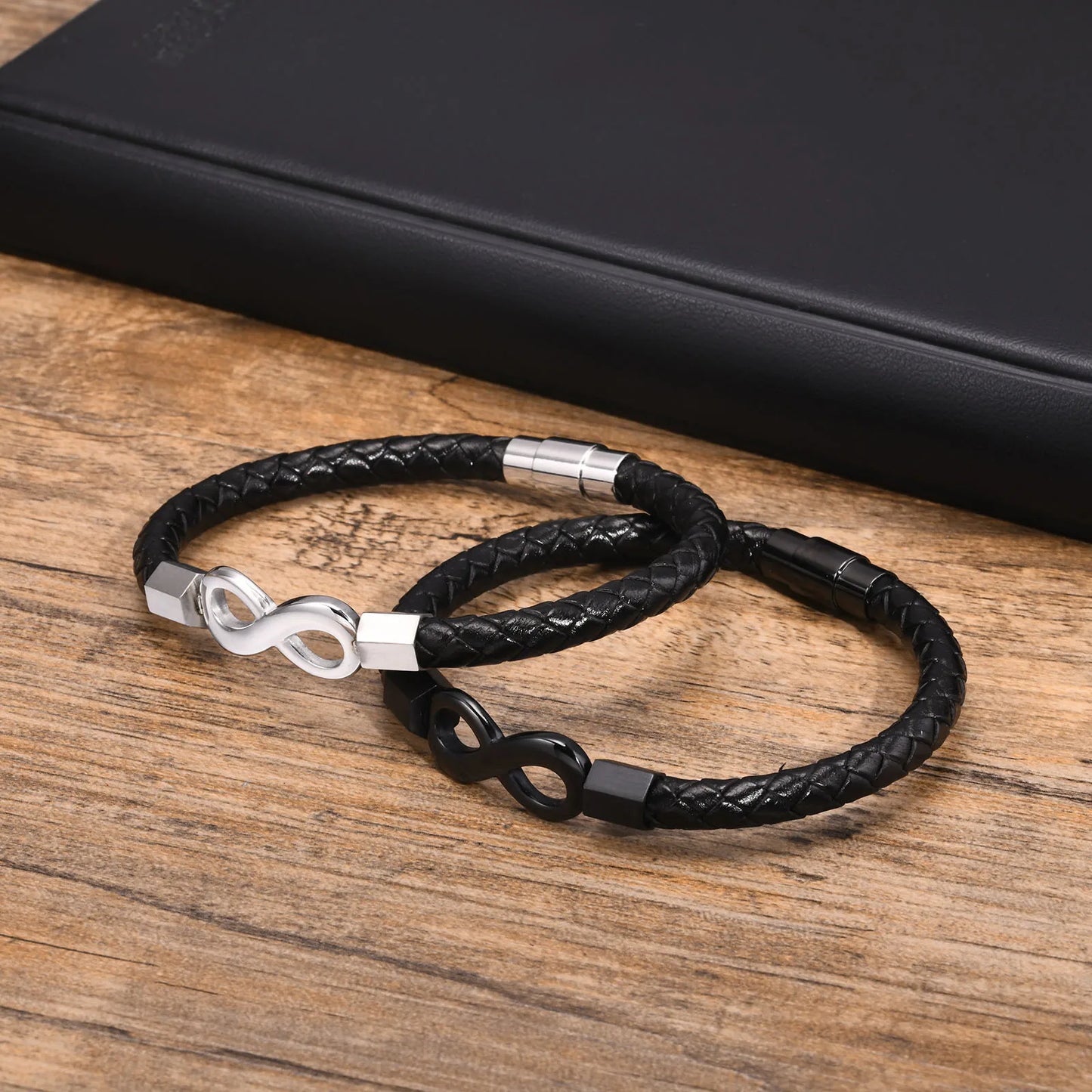 Two black leather bracelets featuring a silver infinity symbol, elegantly intertwined for a stylish accessory look.